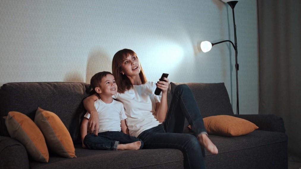Mon and small son sitting on the couch with TV remote in hands and lamp next to them