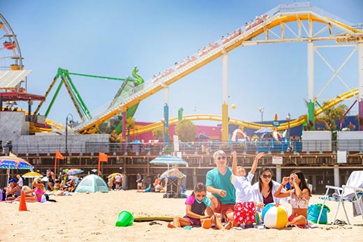 Family with small kids playing in the sand in front of the roller coaster at Santa Monica Pier
